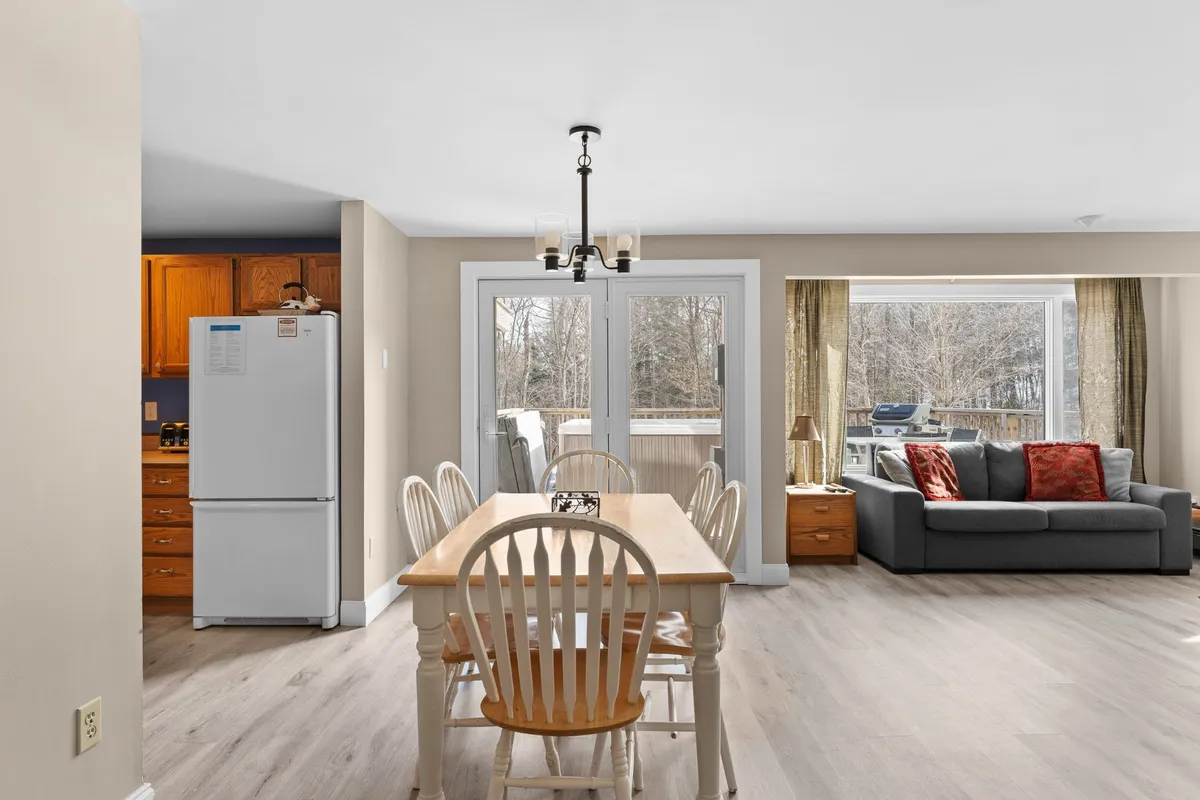 A welcoming, open-concept living and dining area with a dining table, sofa, kitchen elements, and large windows letting in lots of light. The space is perfect for both cooking and relaxing together.