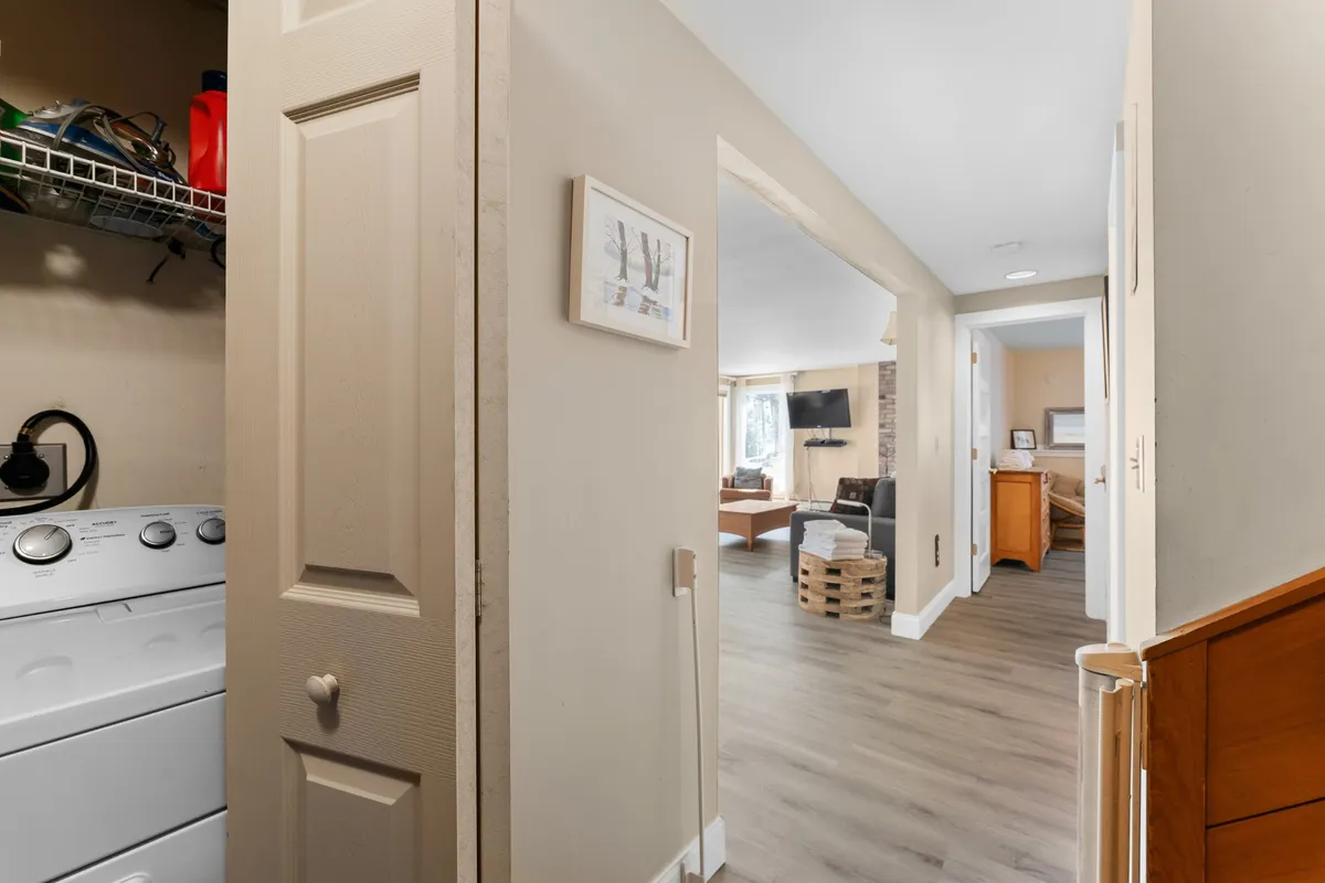 A functional space featuring an in-unit washing machine, framed artwork, and an open doorway leading to a living area. The room balances convenience and comfort, suggesting a home that supports easy living and extended stays.