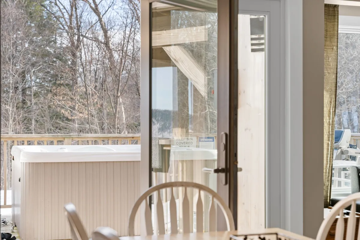 A cozy deck area with an open door leading to a hot tub, wooden deck, and views of surrounding nature. The setup suggests relaxation and shared moments with pets outdoors.