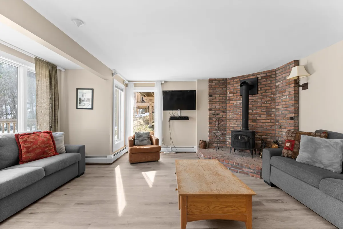 An inviting lounge area centered around a classic wood-burning stove set against a brick wall. Comfortable sofas flank a wooden coffee table, forming a perfect spot for gathering, reading, or sharing stories during chilly evenings.