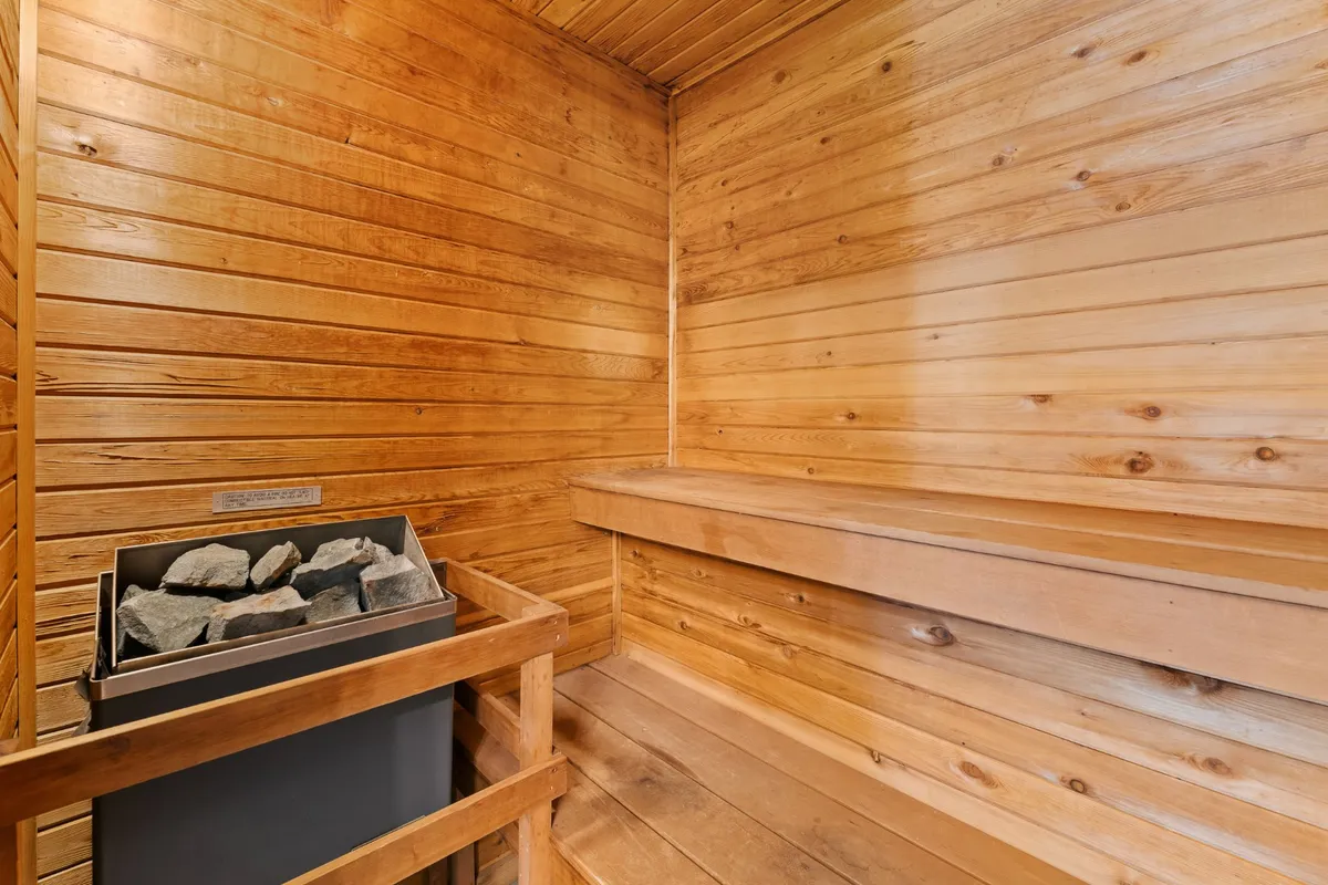 An inviting interior sauna with wooden benches, stone heater, and warm wood paneling. The space is intimate and designed for wellness rituals or moments of solitude, emphasizing relaxation and warmth.