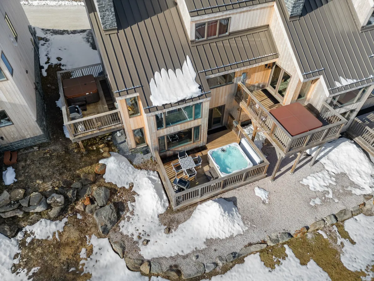 This exterior image showcases a relaxing hot tub on a deck area, surrounded by snow-covered ground and thoughtful stone landscaping. The deck invites guests to unwind outdoors and take in the wintry mountain atmosphere, with enough space for gatherings or quiet moments under the sky.