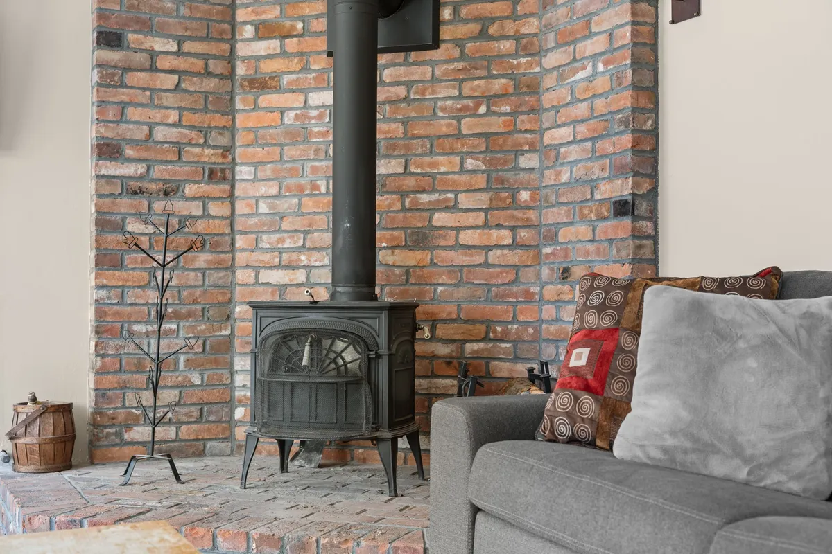 A warm, welcoming living space showcasing a wood-burning stove, a brick accent wall, a comfortable sofa adorned with decorative pillows, and natural touches that enhance the sense of home. The arrangement is perfect for both relaxation and entertaining guests.