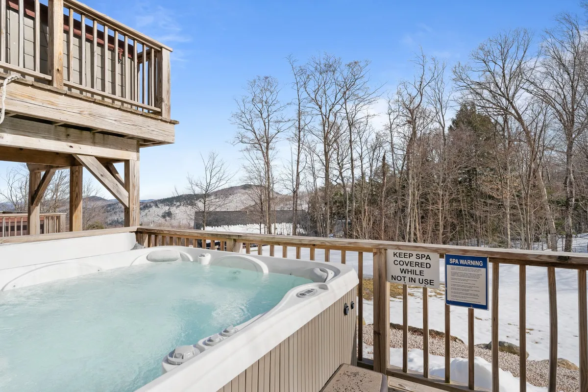 This image captures a wooden deck featuring an outdoor hot tub with expansive mountain views in the background. The scene exudes tranquility, with the hot tub invitingly placed to take in the scenery, and the decking area suggesting space for gatherings and al fresco relaxation.